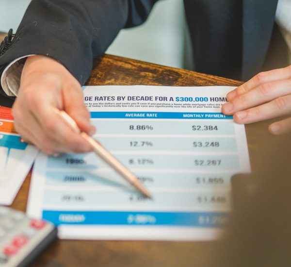 A close-up of hands analyzing mortgage rate documents with a pen and calculator in a business setting.